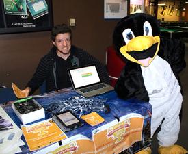 Cal Poly Pomona intern Brandon Sauer posing with another intern wearing the team&#039;s PowerSave mascot, Penny the Penguin, during a tabling event for a national energy savings competition called Campus Conservation Nationals (CCN)