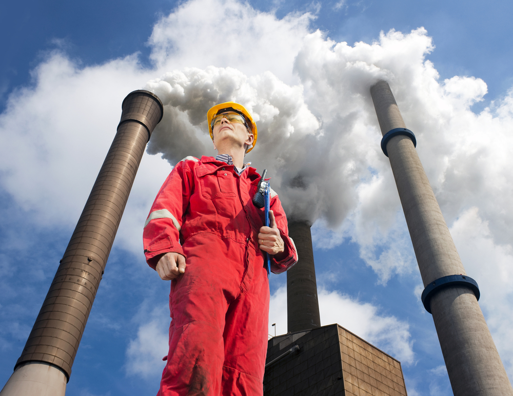 Engineer outside looking up at emissions from power plant.